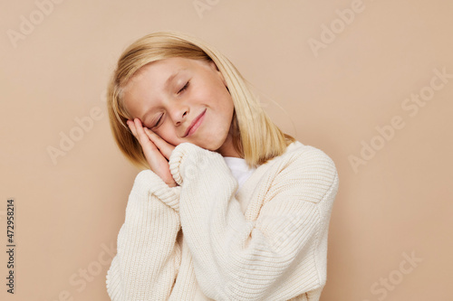 Positive little girl in a sweater, grimaces on a beige background