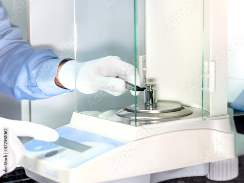 A operator's hand is holding steel calibration weight to place on the analytical balance. Concept of quality control in a laboratory. photo