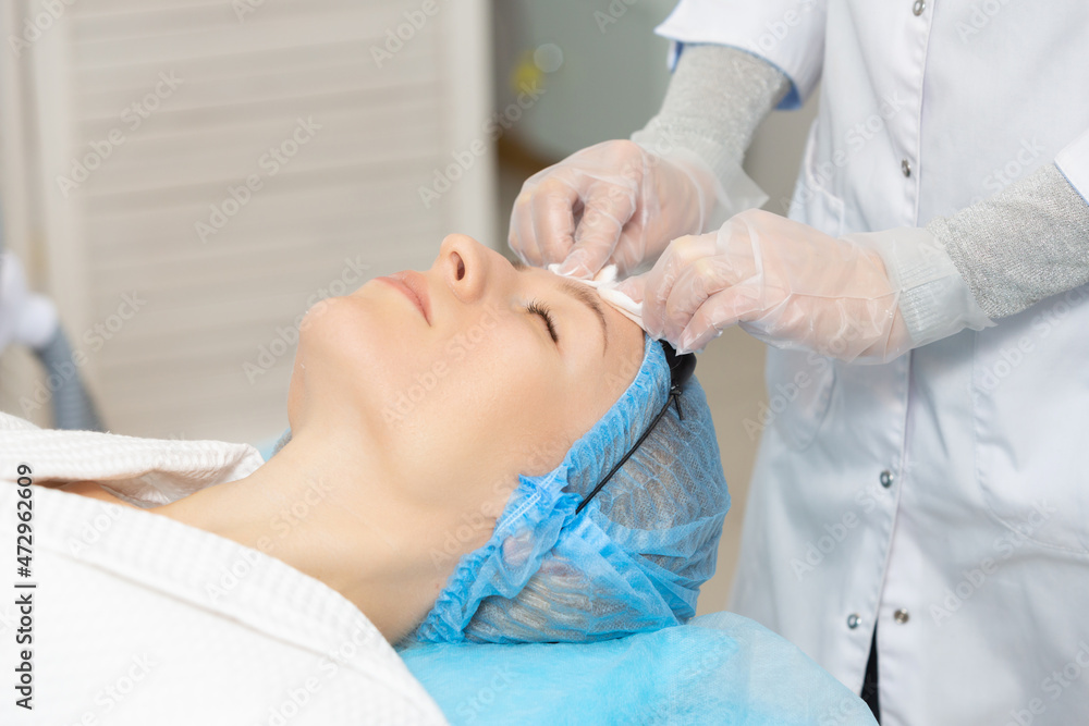 Naklejka premium Photo of professional female cosmetologist using sponges to wash the face of a woman client preparing for a cosmetic procedure. Rejuvenating and moisturizing procedures