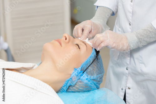 Photo of professional female cosmetologist using sponges to wash the face of a woman client preparing for a cosmetic procedure. Rejuvenating and moisturizing procedures