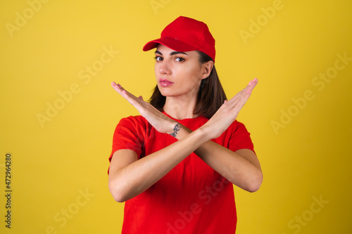 Delivery service worker woman in red cap, blank t-shirt, uniform, work clothes, courier at the service during quarantine, coronavirus covid-19 virus shows stop sign