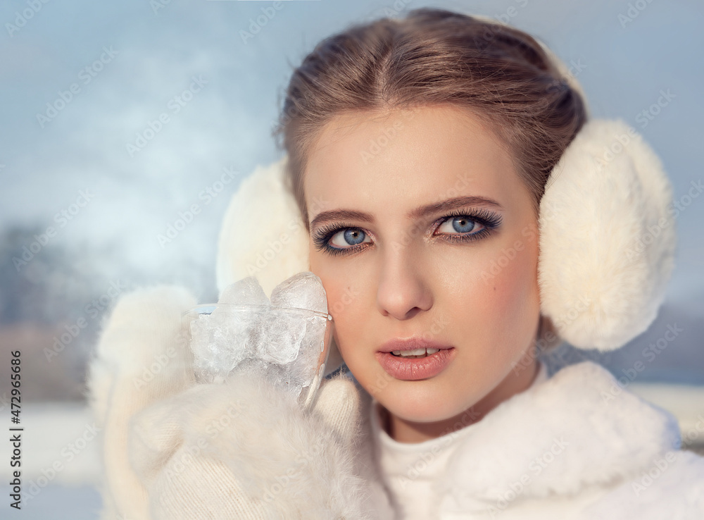 A pretty young blonde teenage woman in a white fur coat, a white pom-pom hat and white mittens holding a steaming clear glass ice cup outdoors on a sunny winter day. Bask in the cold A pretty young blonde teenage woman in a white fur coat, a white pom-pom hat and white mittens holding a steaming clear glass ice cup outdoors on a sunny winter day. Bask in the cold