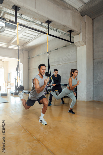 Suspension workout. Coach trains man and woman to do lunge exercise in a gym.