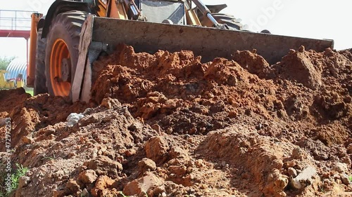 The excavator backfills the pit with the front bucket. Moves soil around the construction site. Close-up. Heavy construction equipment.
