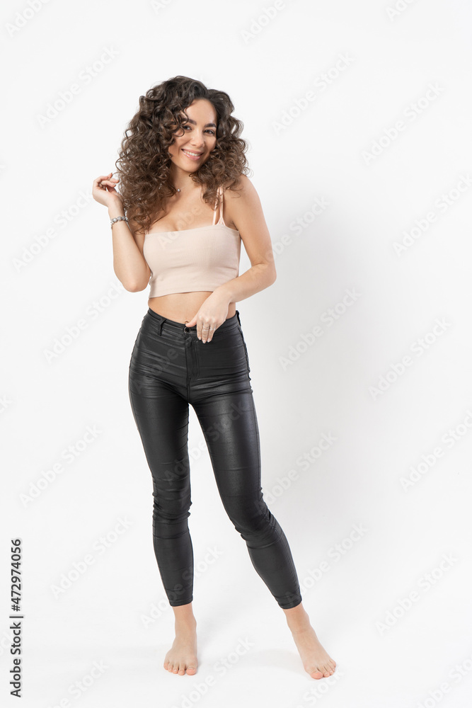 A beautiful young female model with curly long dark hair curled on a curling iron smiles and poses for a portrait on a white background. A beautiful young female model with curly long dark hair curled on a curling iron smiles and poses for a portrait on a white background.