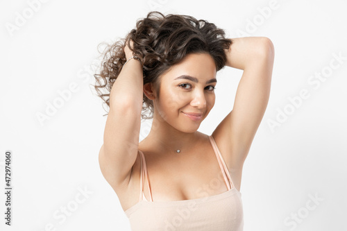 A beautiful young female model with curly long dark hair curled on a curling iron smiles and poses for a portrait on a white background.