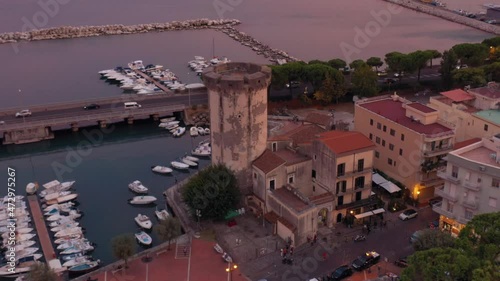 Formia, Torre di Mola, Sunset Aerial Footage - 4K - Flying around the tower and the harbour as cars pass by in the background - Warm sunset colors