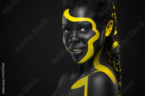 Yellow and black body paint. Woman with face art. Young girl with colorful bodypaint. An amazing afro american model with makeup. photo