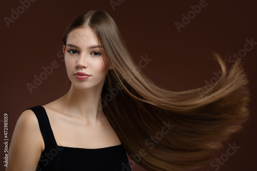 Beautiful young woman with long straight hair and makeup. Brown background