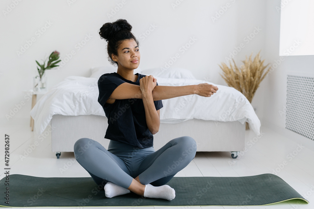 Fototapeta premium African american girl warming up hands sitting on yoga mat