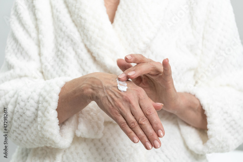 Woman in robe applying moisturizing cream to hands