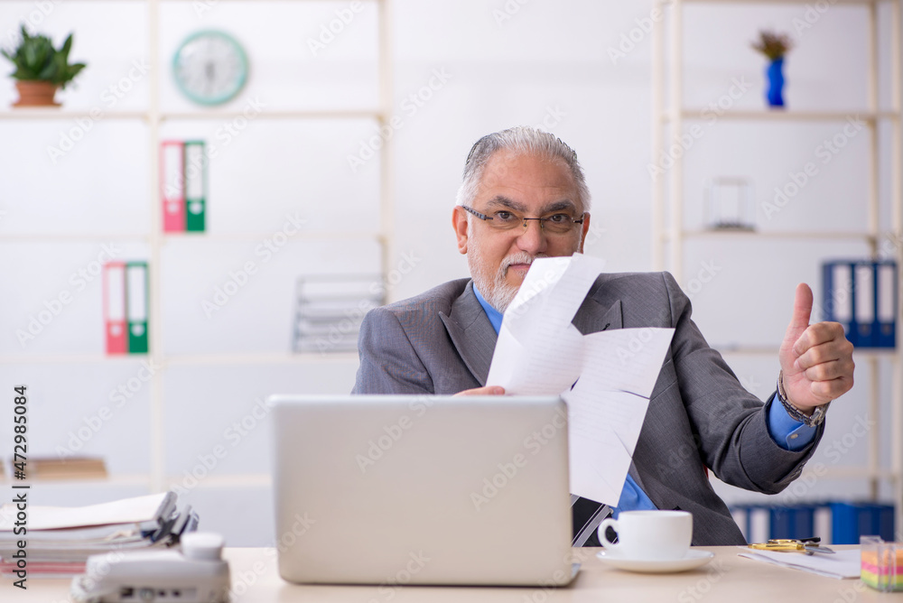 Old male employee holding scissors in the office