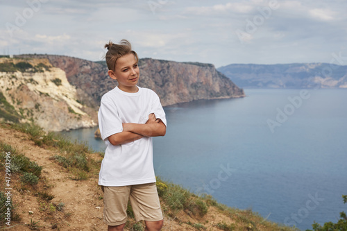 a handsome boy, with flying hair, stands on a rocky seashore © Elena