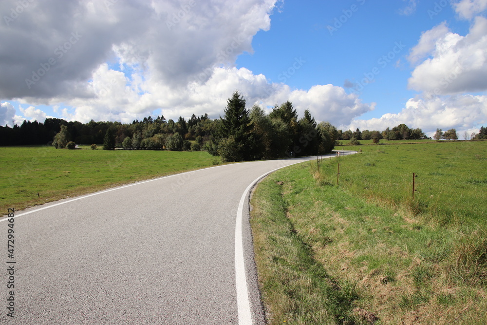 A beautiful wide road in the landscape with blue sky and clouds above near Kaproun, Czech republic
