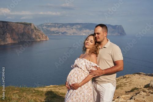 pregnant woman clouds her back on her beloved husband against the background of a beautiful seascape on a sunny summer day