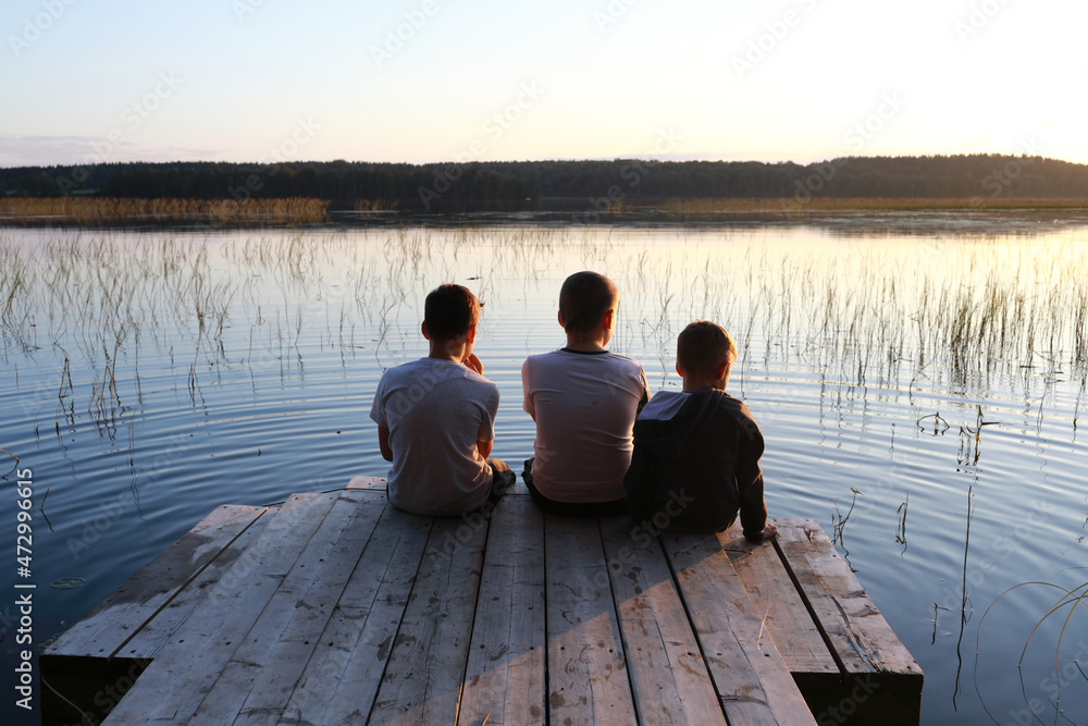 Kids resting on wooden bridge by lake at sunset Kids resting on wooden bridge by lake at sunset