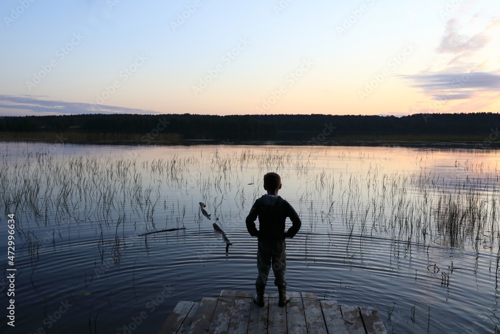 Child standing on wooden bridge by lake at sunset