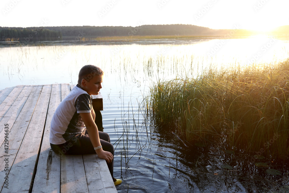 Child resting on wooden bridge by lake at sunset