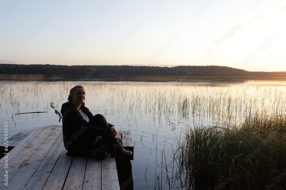 Woman resting on wooden bridge by lake at sunset Woman resting on wooden bridge by lake at sunset