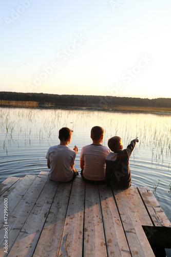 Boys resting on wooden bridge by lake at sunset © Arkady Chubykin