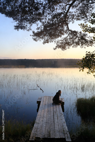 Woman relaxing on wooden bridge by lake at sunset