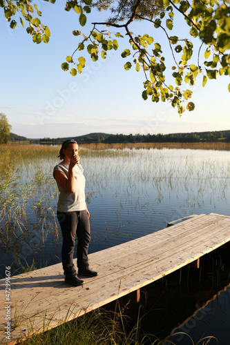 Woman drinking tea on wooden bridge by lake © Arkady Chubykin