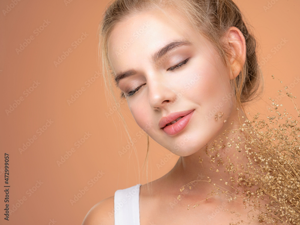 Naklejka premium Calm Blonde girl with a bunch spring dry field flowers near the face - over colored background. Beauty face care concept.