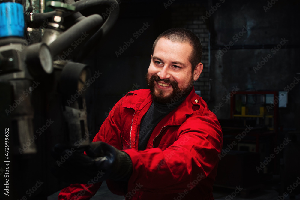 Cheerful bearded male worker operating a machine tool at factory, plant or workshop
