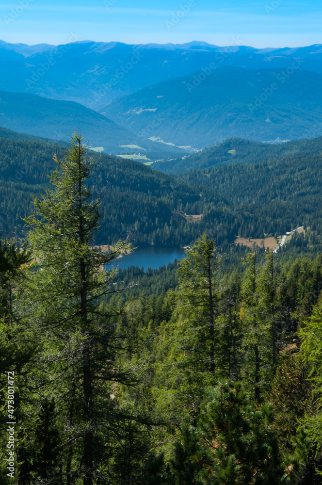 Bergige Landschaft in Österreich.  Blick von einem hochgelegenen Punkt auf  eine Gebirgskette und einem kleinen See im Tal. Sonniger Herbsttag