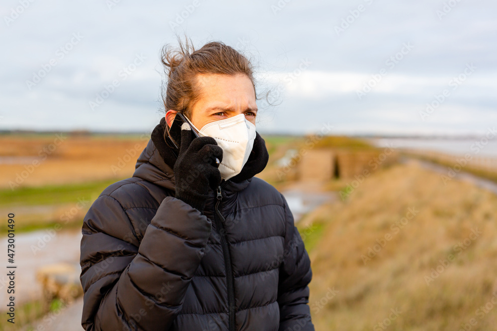 Fototapeta premium A young man wearing a KN95 one use facemask while using his mobile phone during the Covid-19 corona virus pandemic