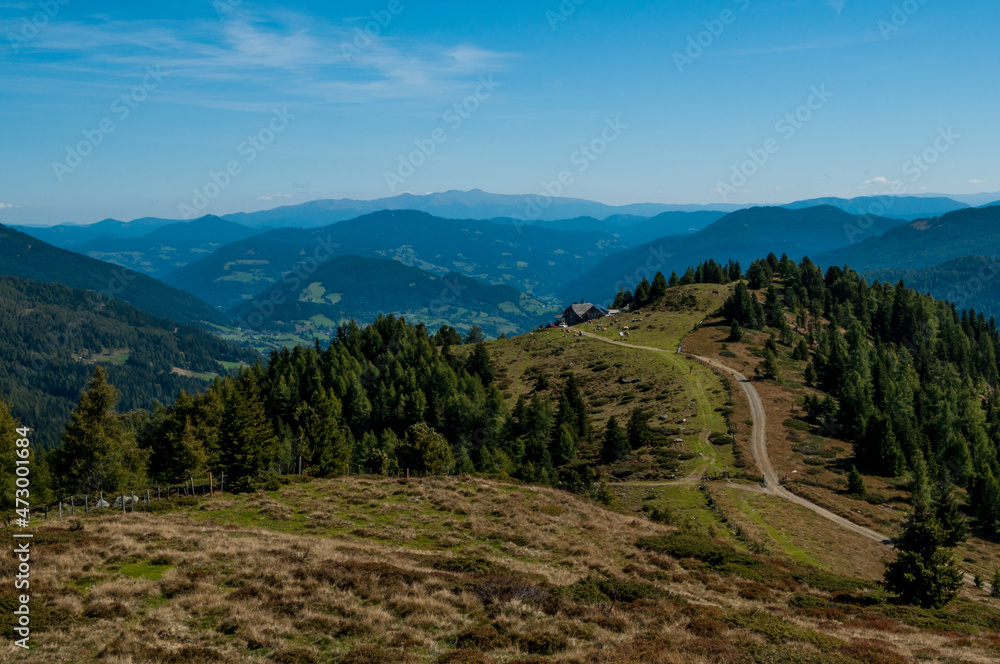 Bergige Landschaft in Österreich . Blick über eine Weide  auf einen Weg, der zu einer Jausenstation führt.  Sonniger Herbsttag