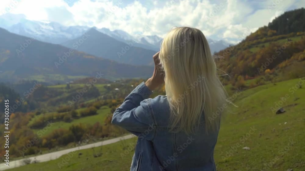 young beautiful slender blonde in a denim jacket straightens her hair and enjoys the nature of the autumn mountain landscape. She looks into distance, at the valley. Mountains, tourists. Slow motion. young beautiful slender blonde in a denim jacket straightens her hair and enjoys the nature of the autumn mountain landscape. She looks into distance, at the valley. Mountains, tourists. Slow motion.