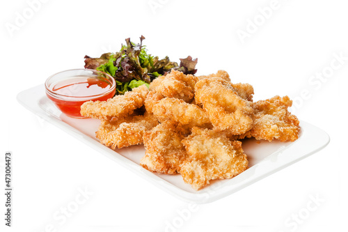 Side view of fried chicken fillet in panko breadcrumbs served with lettuce. sweet and sour sauce in saucepan near dish isolated on white background 