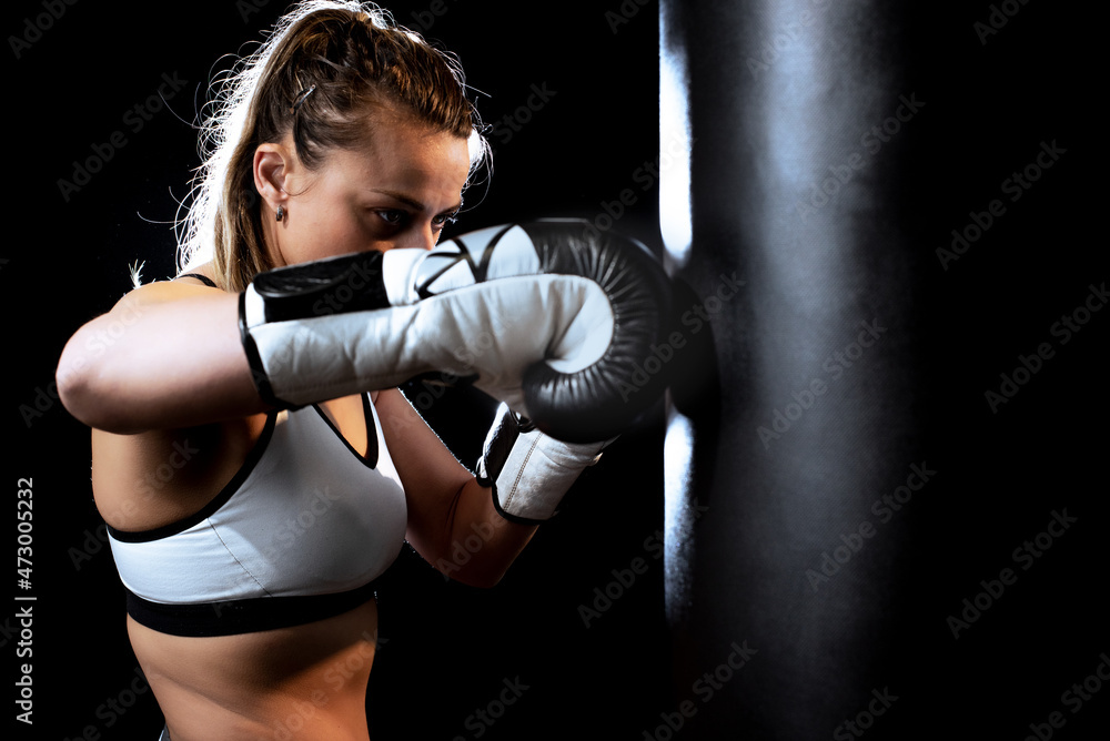 Real boxing girl with boxing bag on black background.