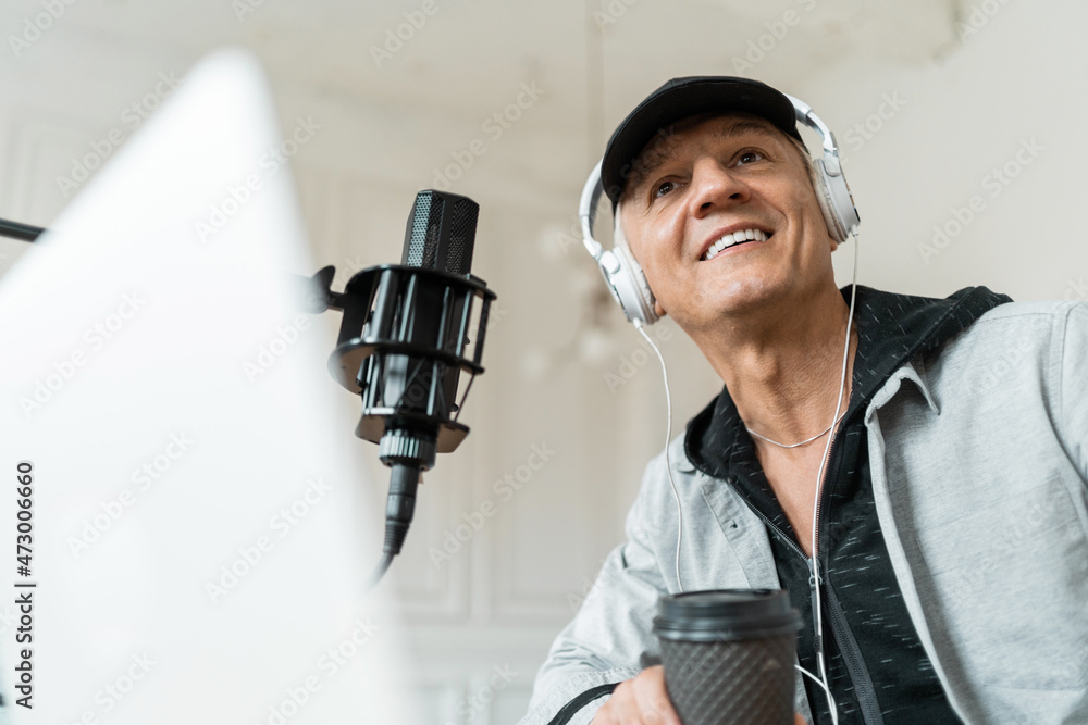 A blogger communicates with people through a microphone. Portrait of a fashionable radio host pro age man working in a recording studio. A blogger communicates with people through a microphone. Portrait of a fashionable radio host pro age man working in a recording studio.