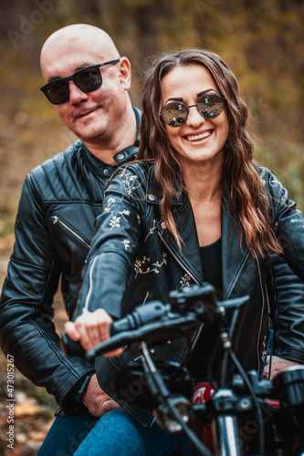 Cute couple near a red motorcycle in the autumn forest. Relationship concept. A pair of bikers in leather jackets. © popovatetiana