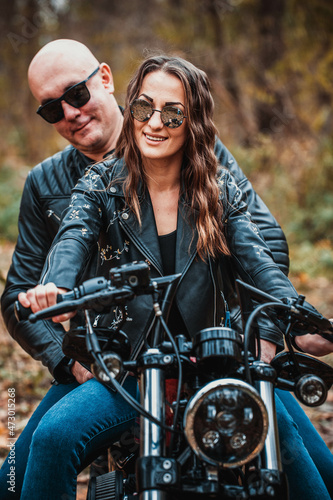 Cute couple near a red motorcycle in the autumn forest. Relationship concept. A pair of bikers in leather jackets.