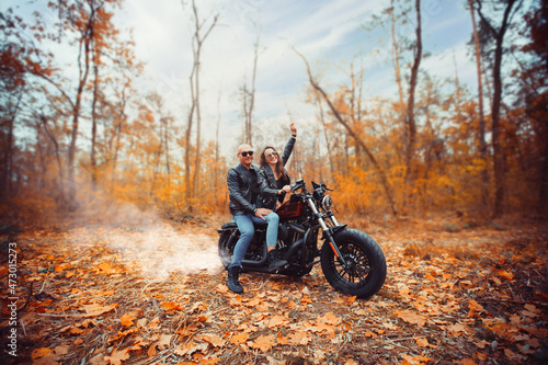 Fototapeta Naklejka Na Ścianę i Meble -  Cute couple near a red motorcycle in the autumn forest. Relationship concept. A pair of bikers in leather jackets.