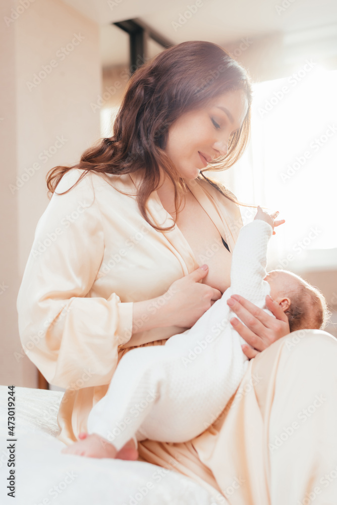 Happy mother breastfeeding her newborn baby while sitting on bed Happy mother breastfeeding her newborn baby while sitting on bed