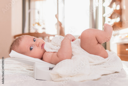 A beautiful newborn girl is weighed on an electronic scale in the bedroom