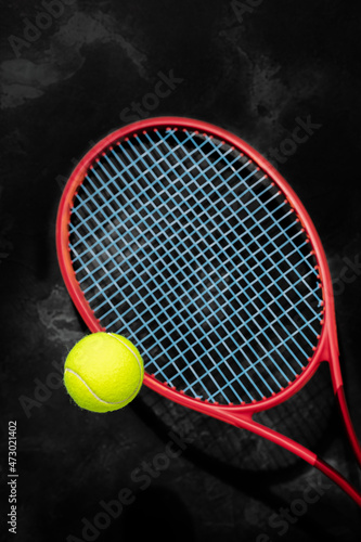 Tennis. Selected focus, sport composition with yellow tennis ball and red racket on a black textured background. The concept of tennis competitions