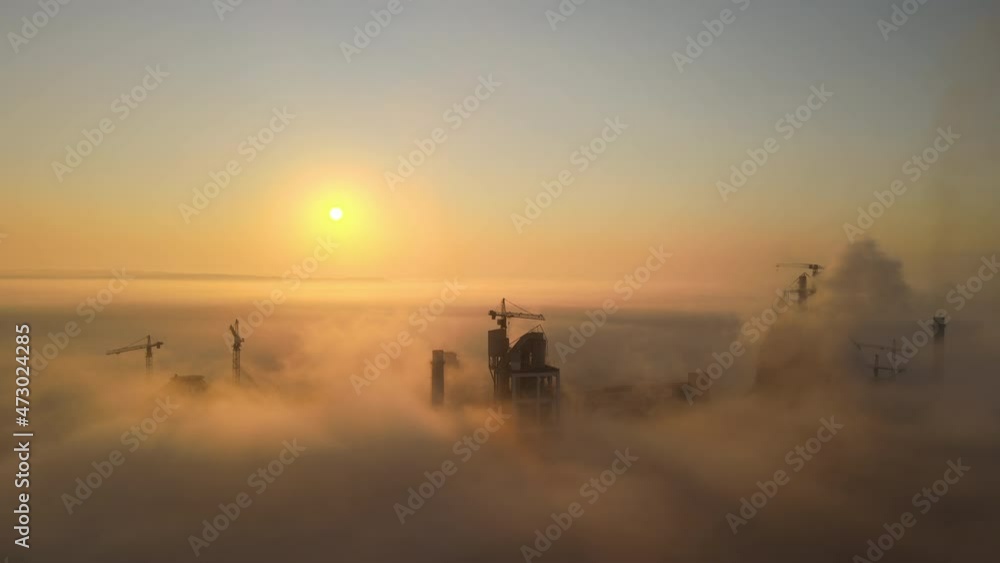Aerial view of cement factory with high concrete plant structure and tower crane at industrial manufacturing site on foggy evening. Production and global industry concept