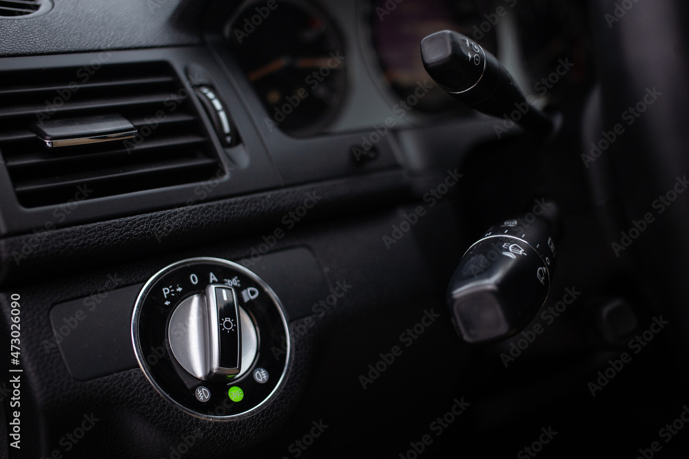 An unrecognizable male driver activates lights or turn signals on the control lever behind the steering wheel of the car.