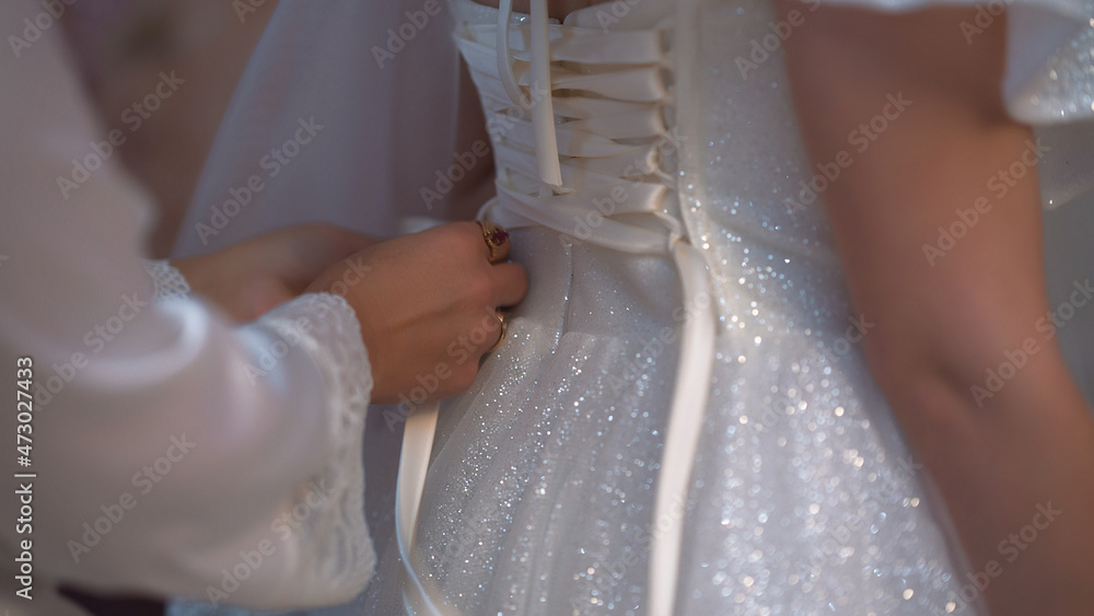 Part of a wedding dress. Hands lace up a white dress. Corset lacing. Part of a wedding dress. Hands lace up a white dress. Corset lacing.