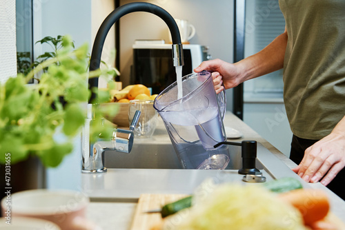 Obraz na płótnie Woman pouring water from faucet into water filter jug at the kitchen
