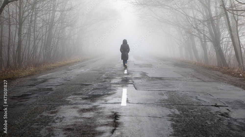 Lonly woman  walk away into the misty foggy road in a dramatic mystic scene.