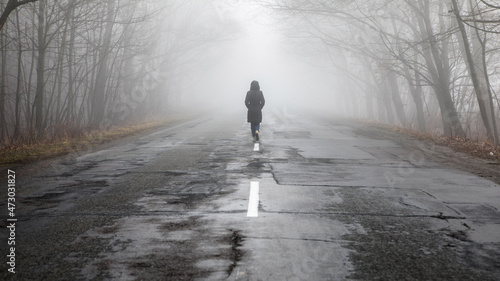 Lonly woman walk away into the misty foggy road in a dramatic mystic scene.