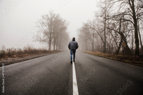 Man walking in a foggy autumn landscape. Lonely man walking in fog. Rural landscape with road in morning mist. Warm autumn colors. Dark mysterious background © Maria