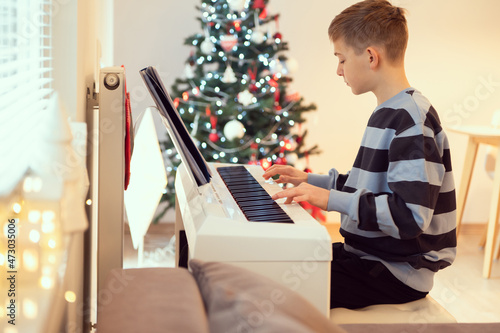 Tennage boy practise plaing piano with new years tree on background