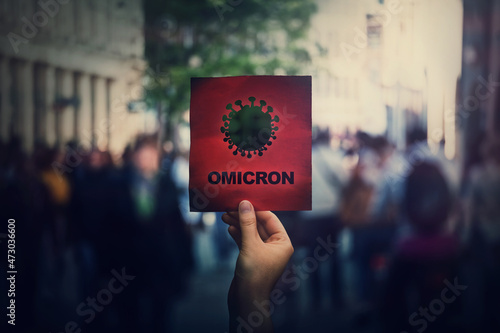 Omicron the new variant of the Covid-19 virus, coronavirus mutations, sars-cov-2 strain. Hand holds red banner warning in the crowded streets. Another wave of pandemic outbreak photo